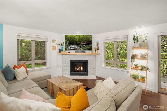 living area featuring a fireplace with flush hearth, baseboards, and wood finished floors