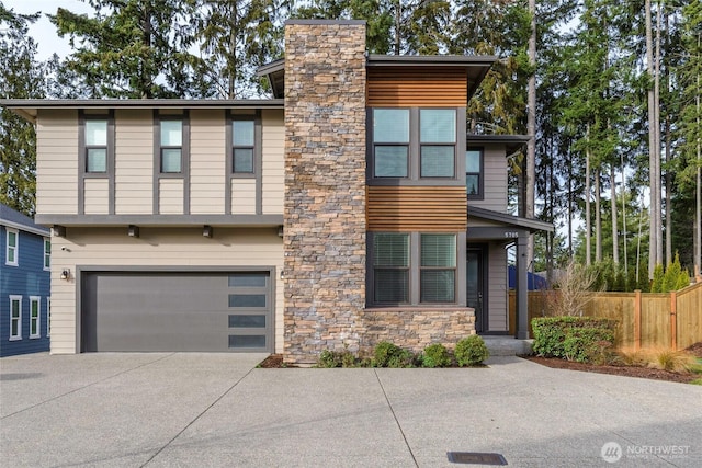 view of front facade featuring driveway, stone siding, a chimney, an attached garage, and fence