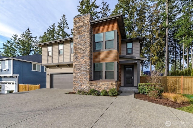 modern home featuring a garage, driveway, stone siding, and fence