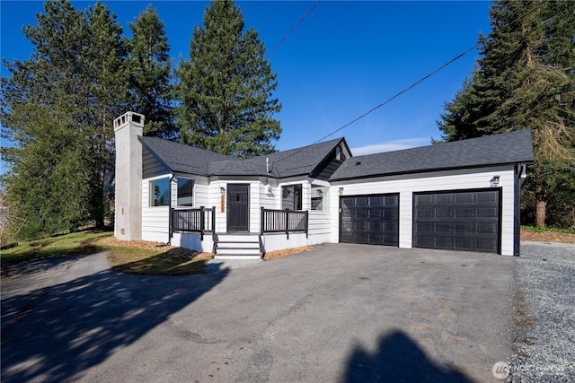 view of front of house featuring driveway, an attached garage, a chimney, and a shingled roof