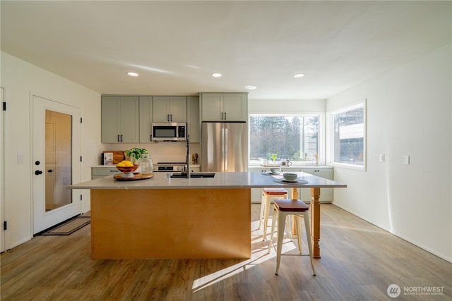 kitchen featuring a kitchen island with sink, stainless steel appliances, light countertops, light wood-type flooring, and gray cabinets