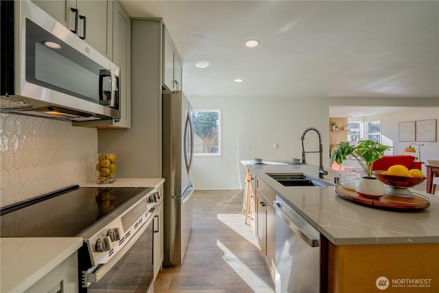 kitchen with appliances with stainless steel finishes, a healthy amount of sunlight, a kitchen island with sink, and a sink