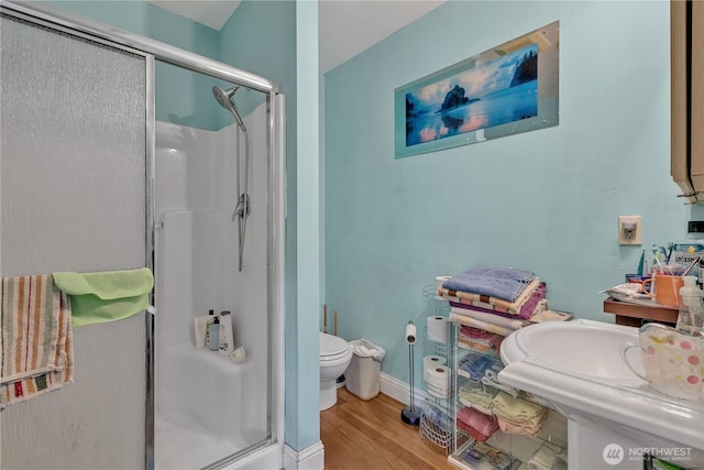 bathroom with a stall shower, baseboards, toilet, and wood finished floors