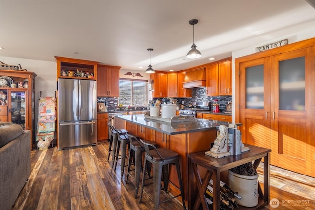 kitchen featuring dark countertops, custom range hood, appliances with stainless steel finishes, dark wood-type flooring, and a kitchen breakfast bar