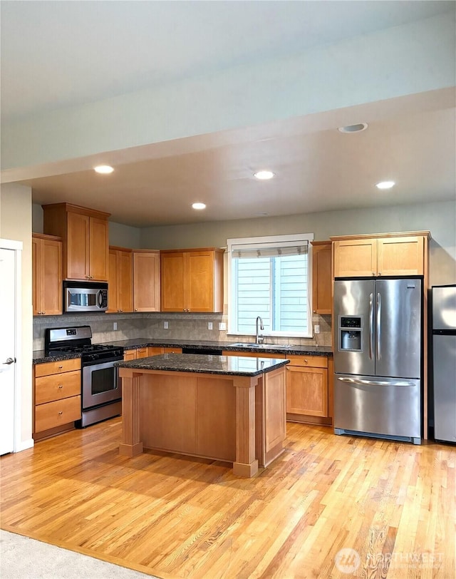 kitchen featuring a kitchen island, a sink, appliances with stainless steel finishes, light wood finished floors, and tasteful backsplash