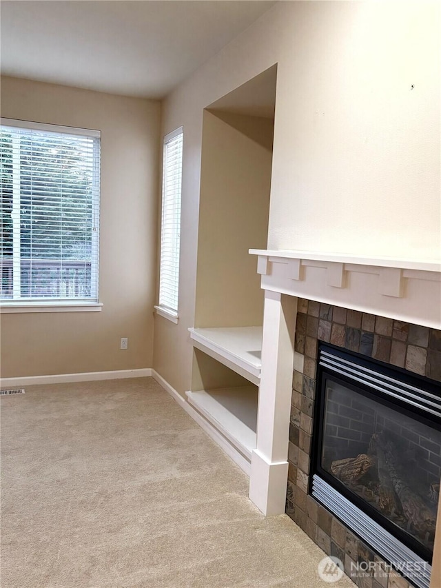 unfurnished living room with carpet floors, a tile fireplace, visible vents, and baseboards