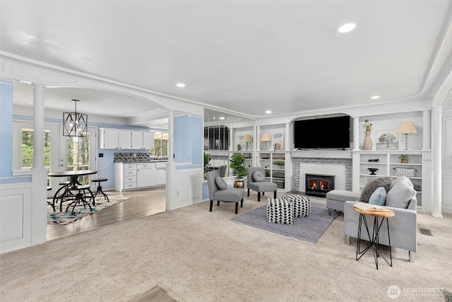 living area with recessed lighting, light colored carpet, decorative columns, and a lit fireplace