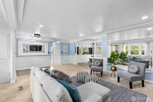 living area featuring arched walkways, recessed lighting, light colored carpet, a decorative wall, and ornamental molding