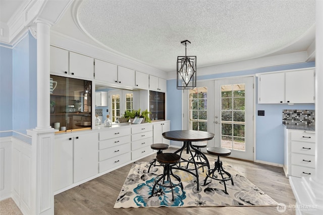 dining room with french doors, ornate columns, crown molding, a textured ceiling, and light wood-style floors