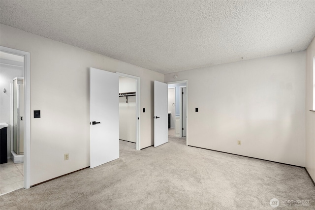 unfurnished bedroom with a walk in closet, light carpet, a textured ceiling, and ensuite bathroom