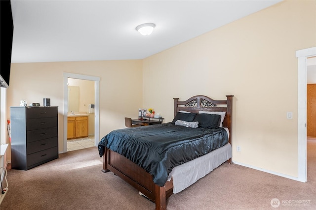 bedroom featuring vaulted ceiling, ensuite bathroom, baseboards, and light colored carpet