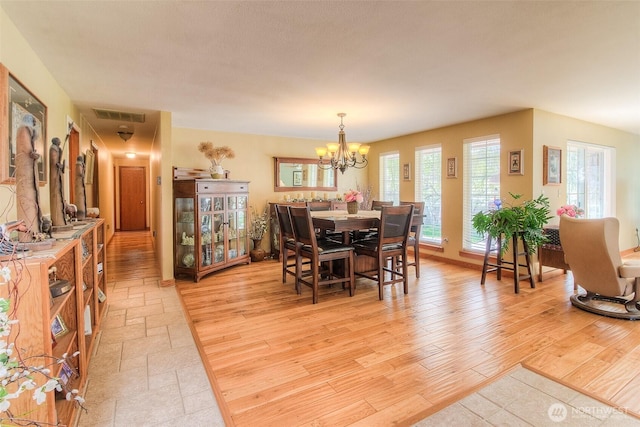 dining room with light wood-style floors, visible vents, and a notable chandelier