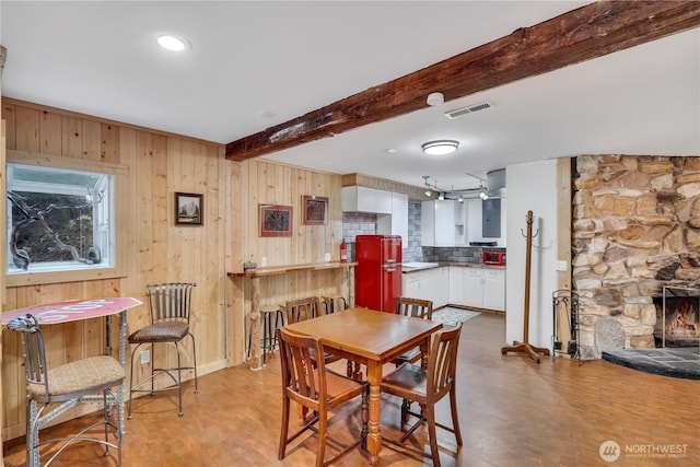 dining area featuring wood walls, visible vents, beam ceiling, and a stone fireplace