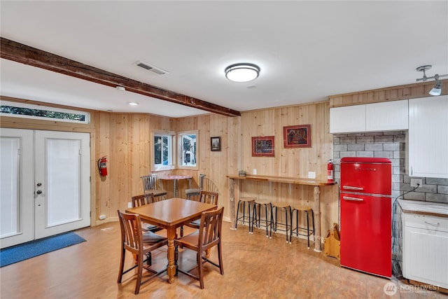 dining room with french doors, visible vents, wooden walls, light wood-type flooring, and beamed ceiling