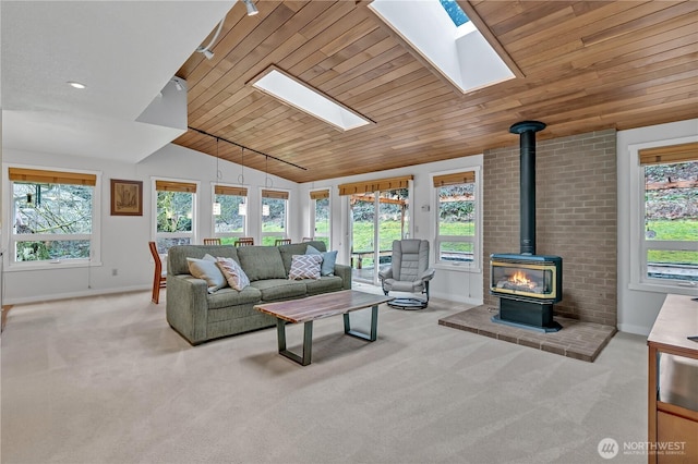 living area with carpet flooring, wood ceiling, baseboards, lofted ceiling with skylight, and a wood stove