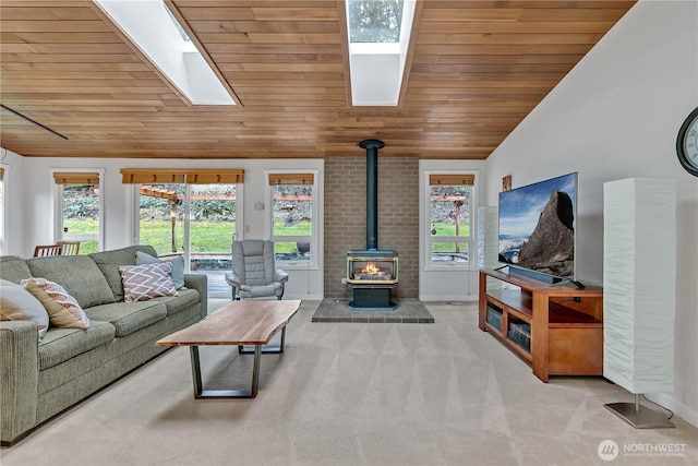 living area featuring vaulted ceiling with skylight, baseboards, wood ceiling, a wood stove, and carpet floors