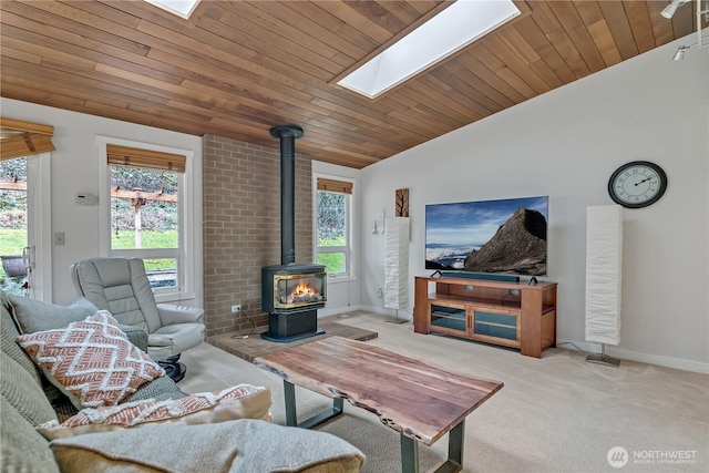 carpeted living room featuring vaulted ceiling with skylight, wooden ceiling, a wood stove, and a healthy amount of sunlight