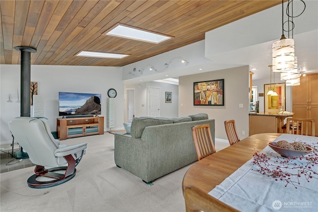 living area featuring light carpet, lofted ceiling with skylight, wood ceiling, and a wood stove