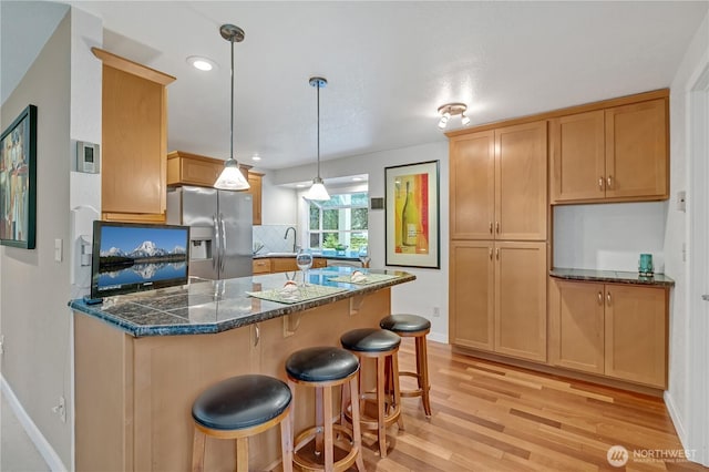 kitchen featuring a sink, stainless steel refrigerator with ice dispenser, backsplash, light wood finished floors, and a kitchen bar