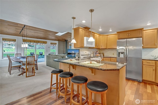 kitchen with pendant lighting, decorative backsplash, white appliances, a peninsula, and a kitchen bar