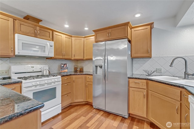 kitchen featuring light wood finished floors, decorative backsplash, a sink, dark stone countertops, and white appliances