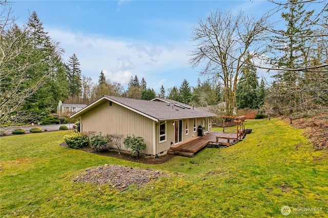 rear view of property with a wooden deck, a shingled roof, and a yard