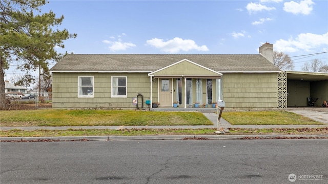 view of front of property featuring an attached carport, a shingled roof, concrete driveway, a front lawn, and a chimney