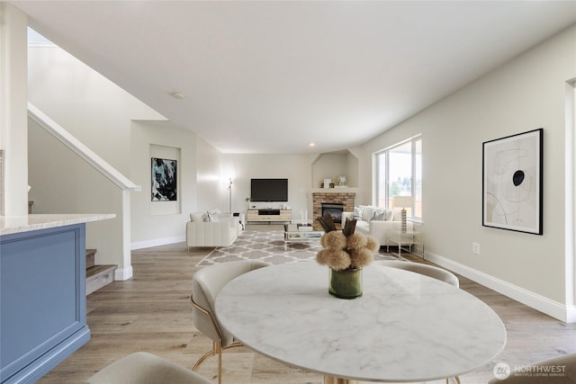 dining space with light wood-type flooring, stairway, baseboards, and a fireplace