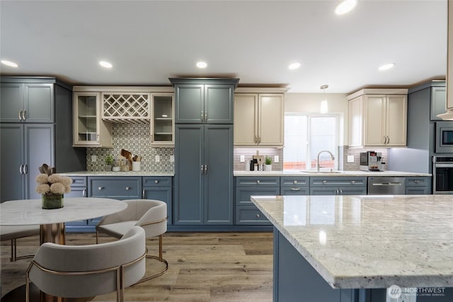 kitchen featuring light wood finished floors, recessed lighting, a sink, glass insert cabinets, and appliances with stainless steel finishes