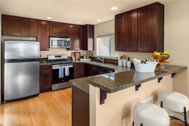 kitchen with stainless steel appliances, a sink, dark brown cabinets, light wood-type flooring, and a peninsula