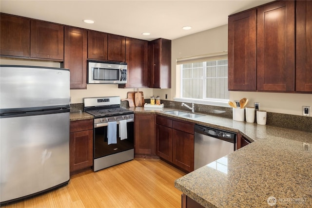 kitchen with appliances with stainless steel finishes, a sink, light wood-style flooring, and dark stone countertops