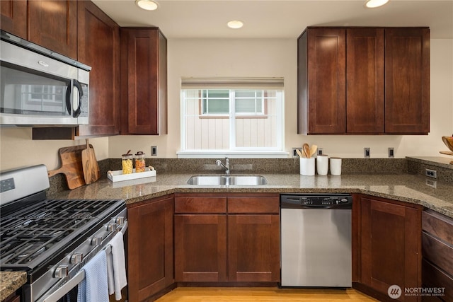 kitchen featuring appliances with stainless steel finishes, dark stone counters, a sink, and recessed lighting