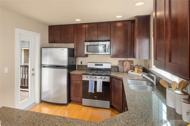 kitchen with dark brown cabinetry, dark stone countertops, stainless steel appliances, a sink, and recessed lighting