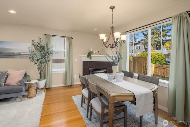 dining area featuring recessed lighting, light wood-style flooring, an inviting chandelier, a tile fireplace, and baseboards