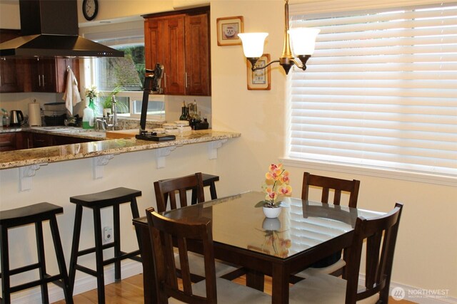 kitchen with white cooktop, light wood-style floors, light stone countertops, a kitchen breakfast bar, and exhaust hood