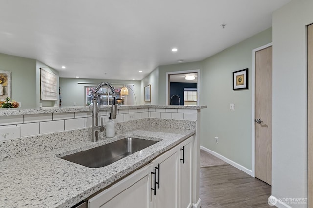 kitchen featuring a sink, light stone counters, recessed lighting, white cabinets, and baseboards