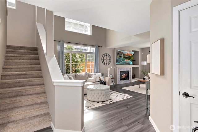 living area featuring visible vents, a glass covered fireplace, wood finished floors, baseboards, and stairs