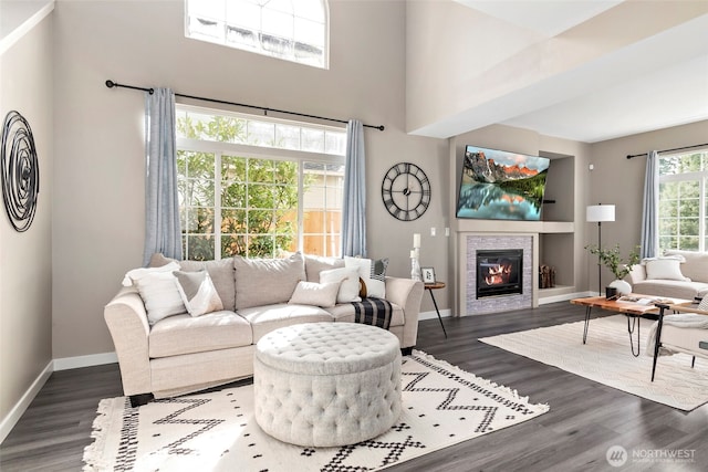 living room with a high ceiling, a tiled fireplace, baseboards, and wood finished floors