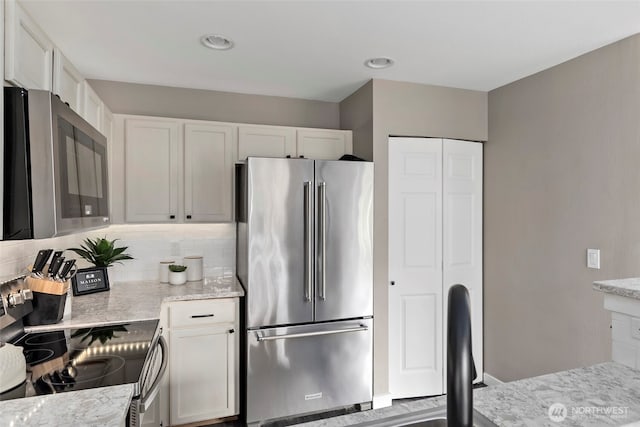 kitchen with appliances with stainless steel finishes, white cabinetry, light stone counters, and decorative backsplash