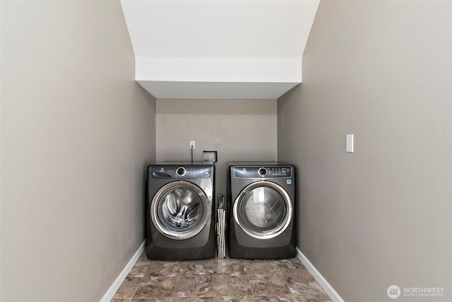 washroom featuring laundry area, baseboards, stone finish flooring, and washing machine and clothes dryer