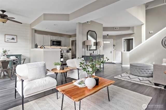 living area featuring light wood finished floors, visible vents, baseboards, ceiling fan, and wood walls