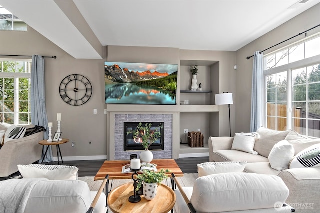 living area featuring a glass covered fireplace, a healthy amount of sunlight, baseboards, and wood finished floors