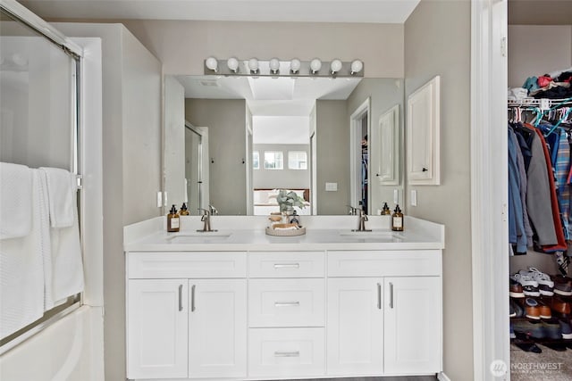 bathroom featuring double vanity, a stall shower, a sink, and a walk in closet