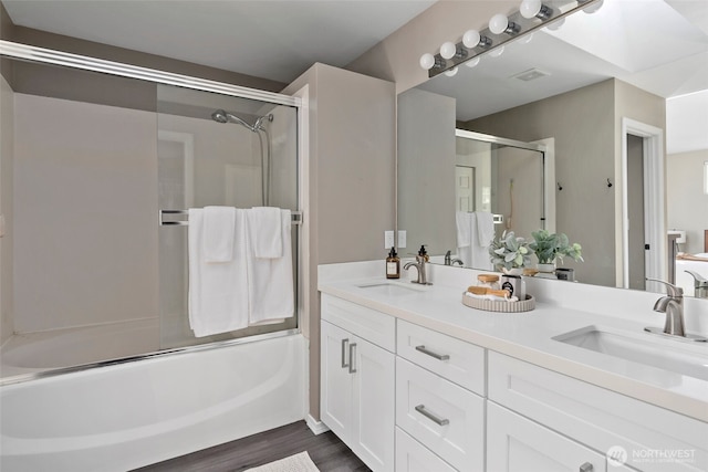 full bath with double vanity, enclosed tub / shower combo, a sink, and wood finished floors