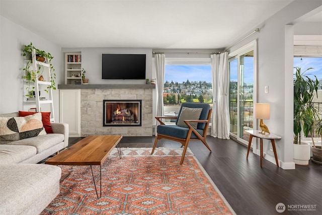 living area with a glass covered fireplace, baseboards, and wood finished floors