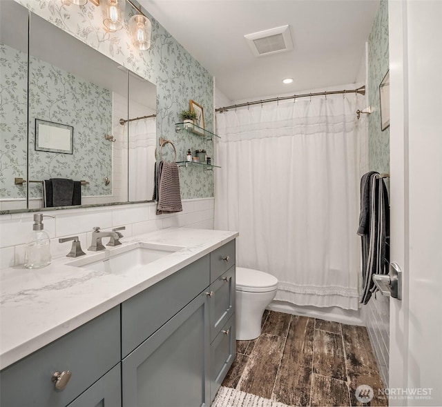 full bathroom featuring toilet, wood finish floors, visible vents, vanity, and wallpapered walls