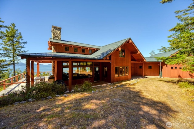 back of property with a standing seam roof, metal roof, and a chimney