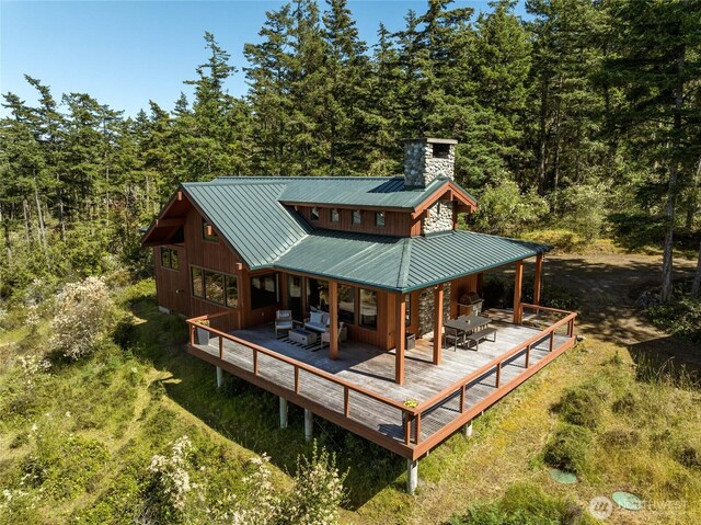 707 NW Thatcher Pass Rd, Decatur Island, WA 98221 - rear view of property featuring a view of trees, a chimney, a wooden deck, a standing seam roof, and metal roof
