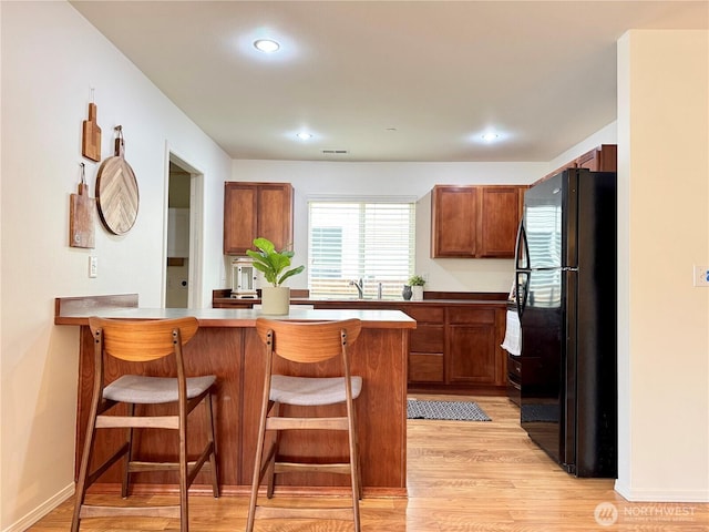 kitchen with light wood finished floors, a breakfast bar, a peninsula, freestanding refrigerator, and a sink