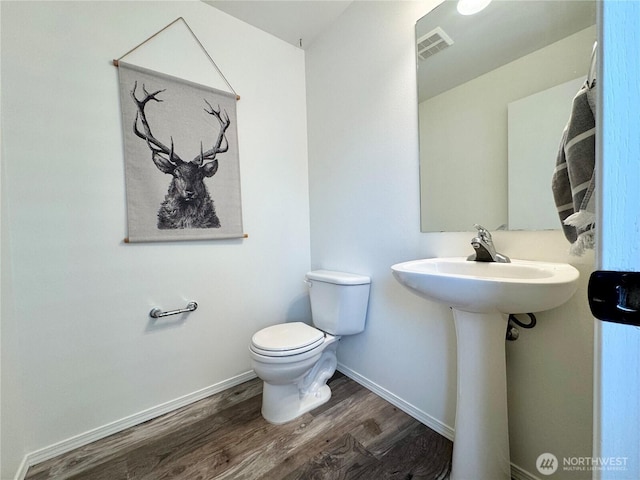 half bathroom with visible vents, baseboards, toilet, and wood finished floors